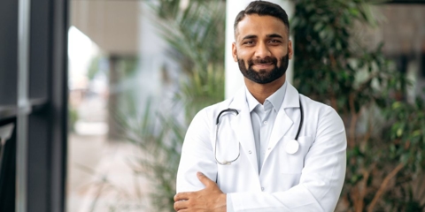 Portrait of an Indian professional therapist in medical uniform and stethoscope, standing in hospital on blurred background after he received help from Sarpa Law.