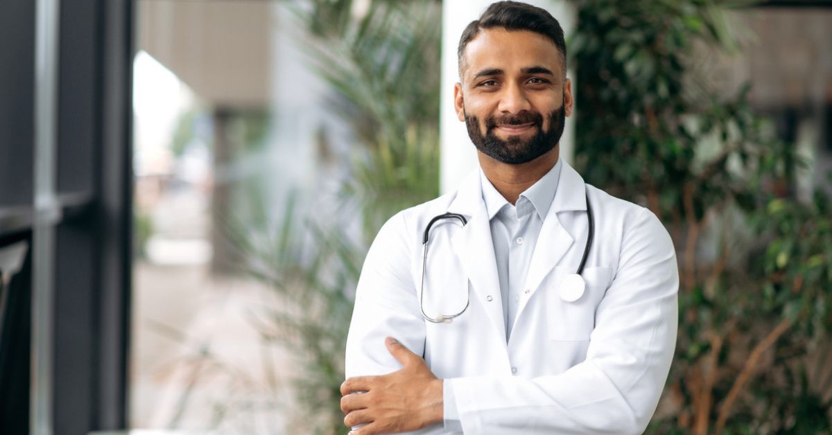 Portrait of an Indian professional therapist in medical uniform and stethoscope, standing in hospital on blurred background after he received help from Sarpa Law.